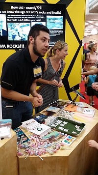 Two students, presenting at a table, in front of a poster about the age of Earth